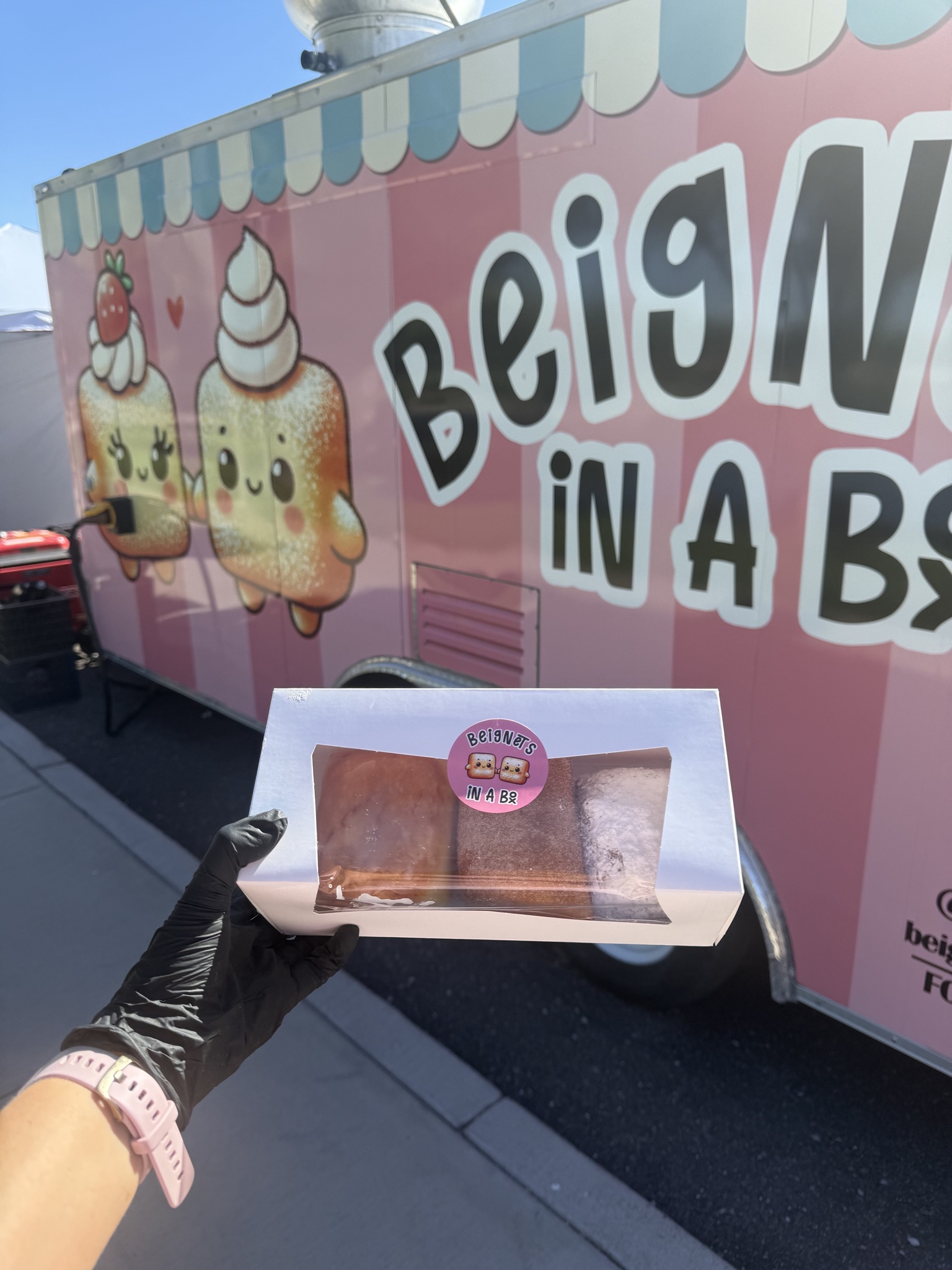 A box of beignets held in front of the pink Beignets in a Box trailer