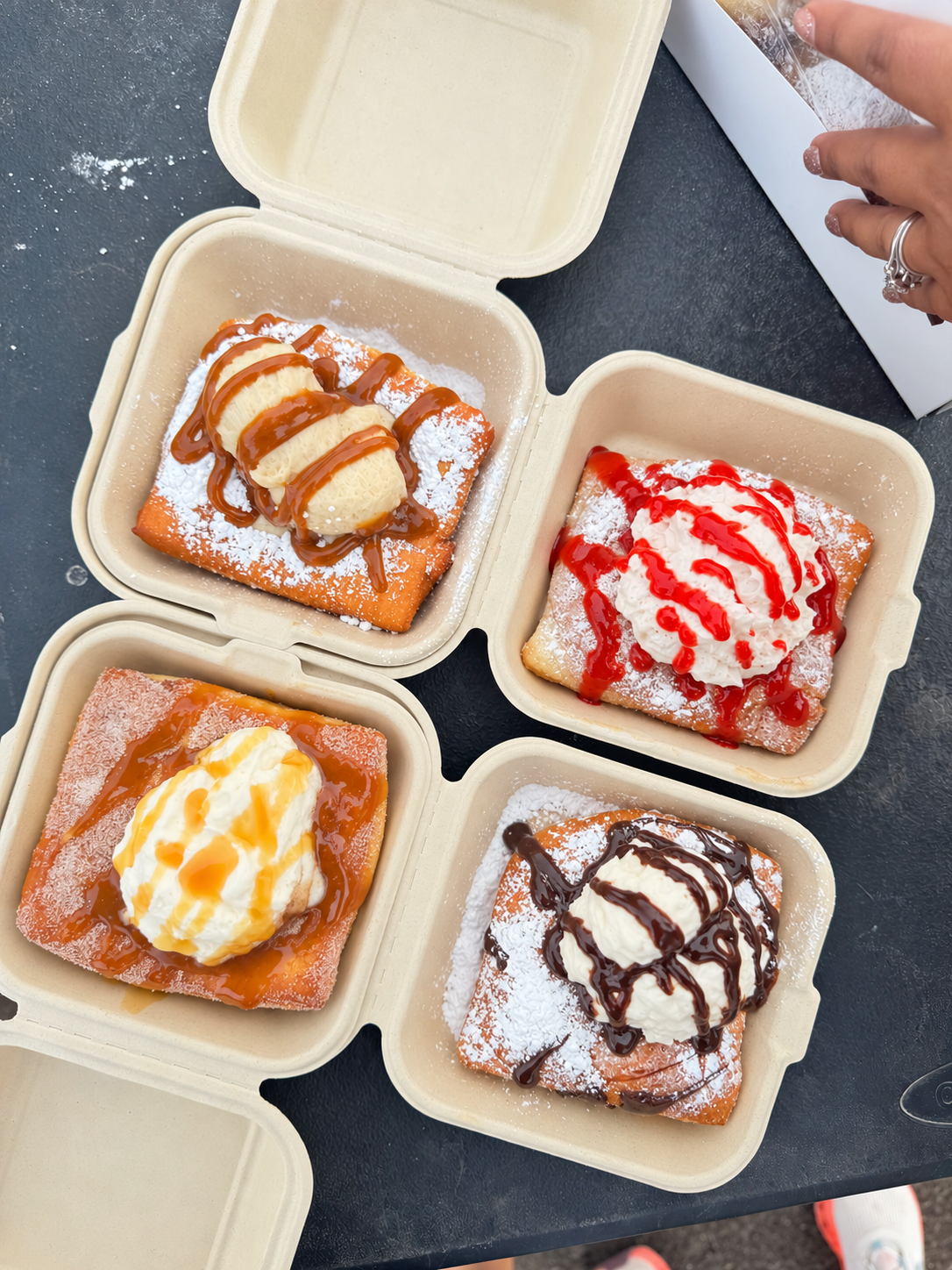 An assortment of four specialty beignets topped with whipped cream and cookie butter, strawberry, caramel, and chocolate drizzles