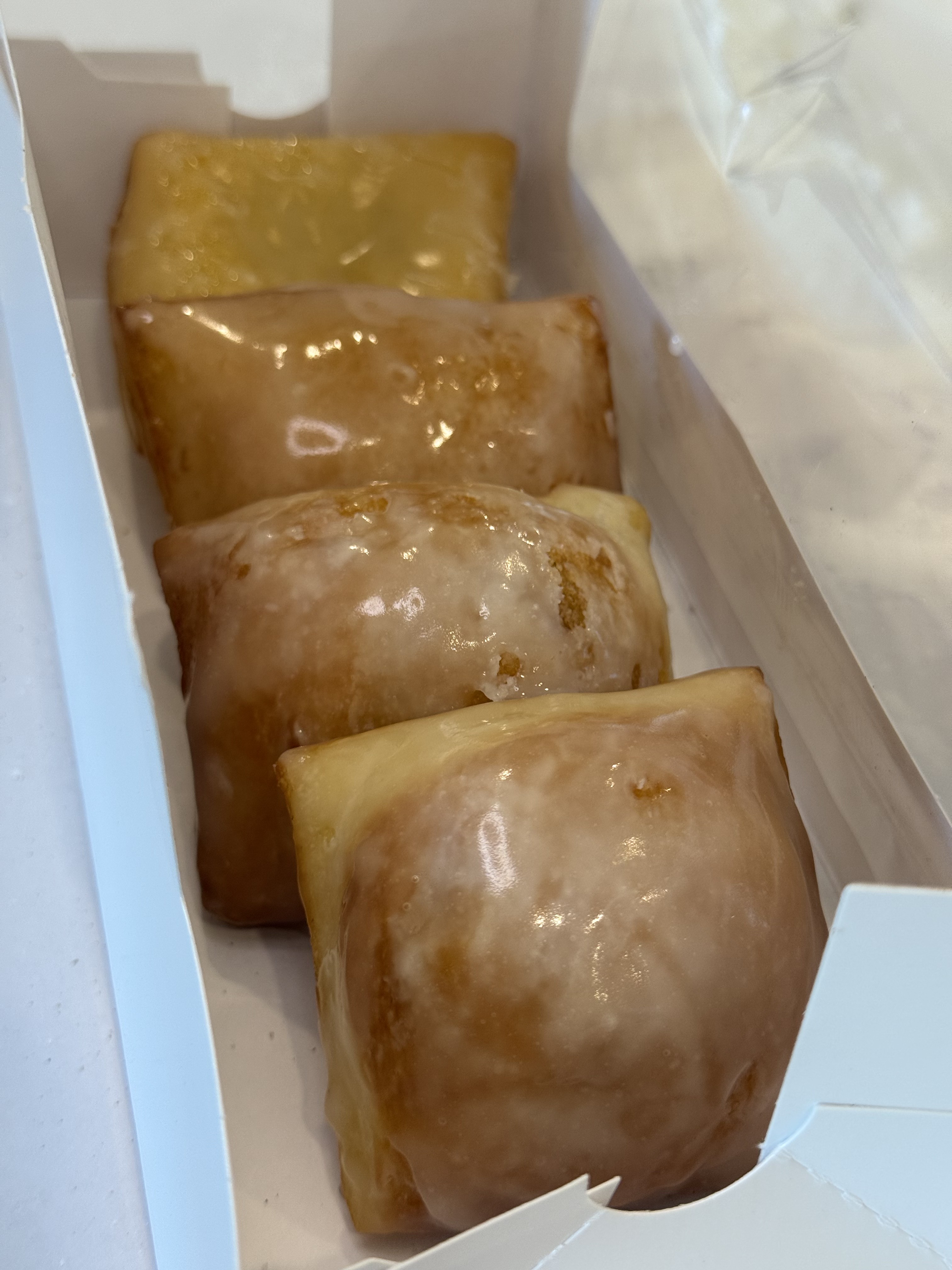 Glazed beignets in an open pastry box